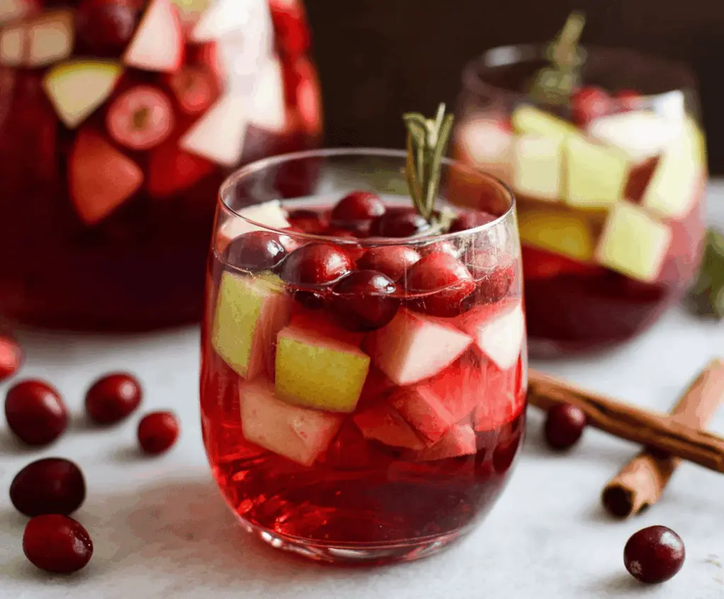 A glass of vibrant cranberry apple sangria garnished with fresh fruit slices, perfect for a cozy fall party celebration.