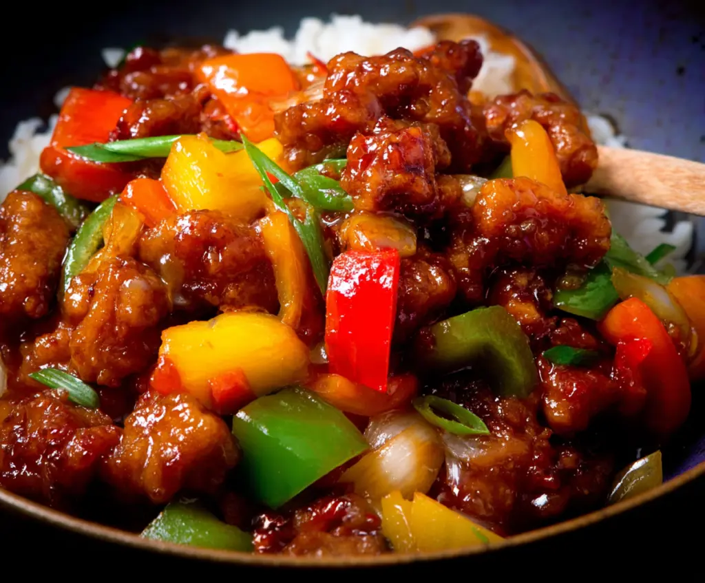 Delicious sweet and sour pork dish with crispy pork chunks, colorful bell peppers, and pineapple served on a white plate.